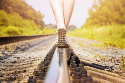Una persona andando de espaldas sobre las vías del tren, en la imagen solo se ve la mitad de las piernas