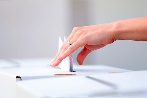 Primer plano de una mano femenina introduciendo un voto en una urna electoral