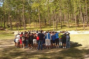 Grupo de jóvenes hacen un circulo en una esplanada dentro de un bosque