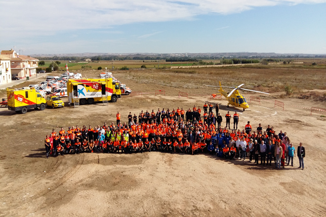 Fotografía desde el aire de un grupo de personas voluntarias, con el helicóptero y varios vehículos de emergencias al fondo