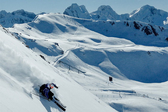 Esquiador baja por una ladera nevada en un paisaje montañoso.