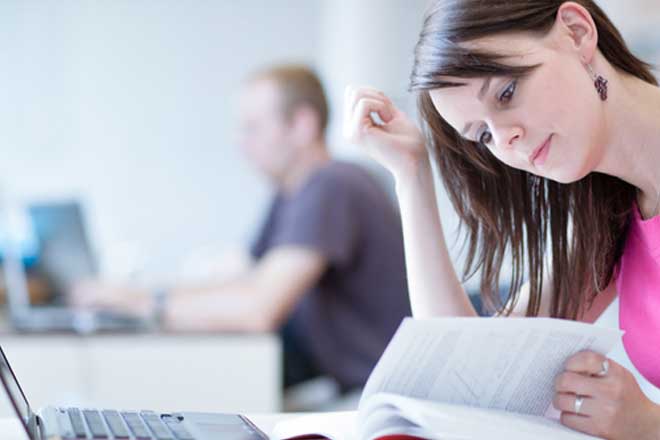Mujer consultando un libro y trabajando con un ordenador portátil en una sala luminosa