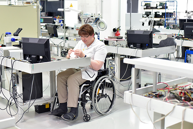 Trabajador discapacitado en silla de ruedas que ensambla componentes electrónicos en una fábrica moderna en el lugar de trabajo
