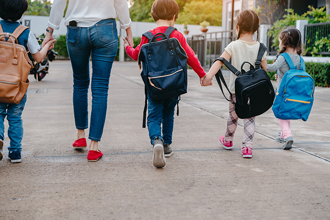 Mujer andando llevando de la mano a un niño y niña al colegio