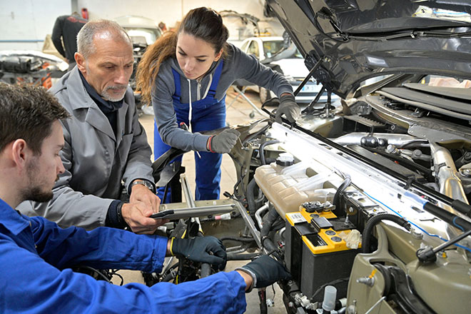Instructor de mecánica mostrando a una alumna y un alumno la batería de un motor de coche