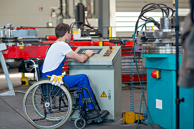 Chico en silla de ruedas manejando una máquina en una fábrica