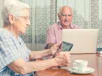 Una pareja de personas mayores, la mujer con una tablet y el hombre con un ordenador