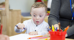 Un niño con síndrome de Down con un lápiz de color azul en la mano