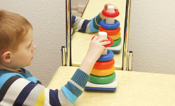 Niño jugando frente a un espejo a apilar aros de diferentes tamaños y colores