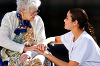 Una mujer agachada coge la mano de una persona mayor sentada.
