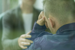 Una persona de espaldas se sujeta la cabeza con la mano, mientras otra persona le toca el brazo en señal de apoyo