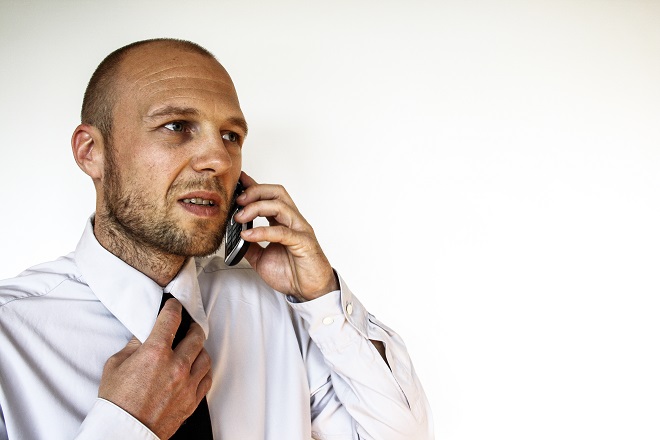 Hombre hablando por el teléfono móvil y con la otra mano desabrochándose la corbata, con síntomas de estrés.