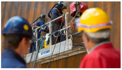 Imagen de dos trabajadores con casco que observan a otros dos que portan protección respiratoria