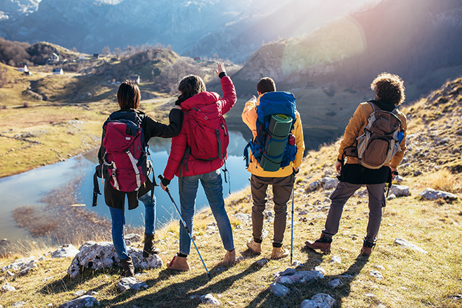 4 jovenes en un paisaje montañoso ven al fondo un lago y unas montañas.