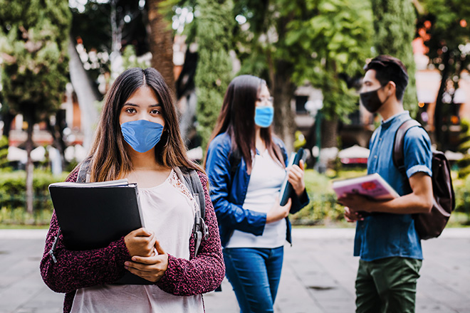 Personas jóvenes, manteniendo la distancia, paseando por la calle con mascarillas