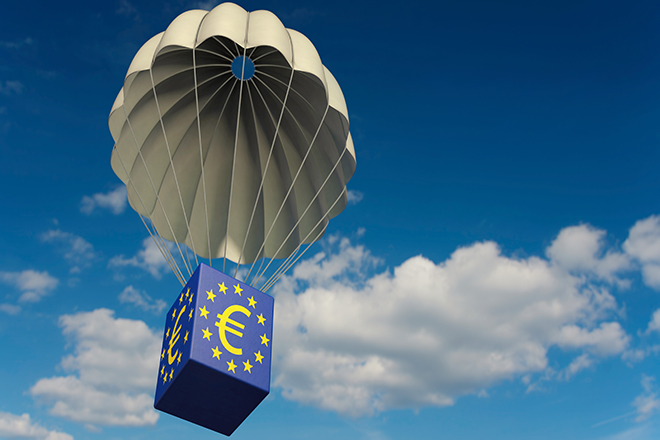 Sobre el cielo planea un paracaídas con el símbolo de la Unión Europea del que cuelga un paquete forrado con el símbolo del euro.
