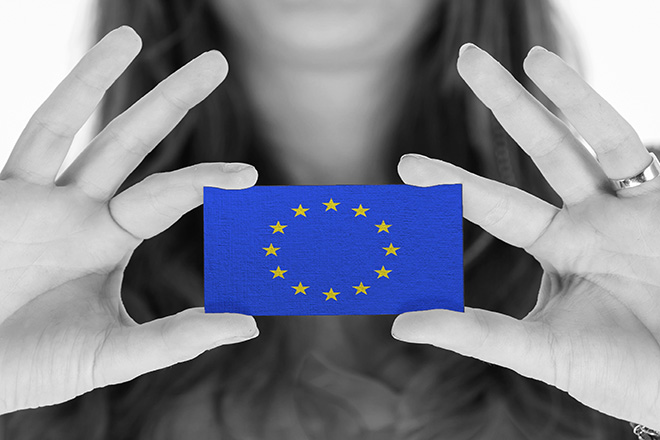 Primer plano de unas manos femeninas en blanco y negro sosteniendo la bandera de la Unión Europea.