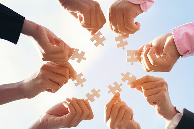 Manos que sujetan piezas de puzzles, intentan unirlas, juntándolas en el centro