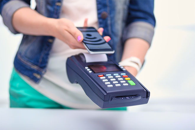 Mujer pagando en un comercio con su móvil en un datáfono