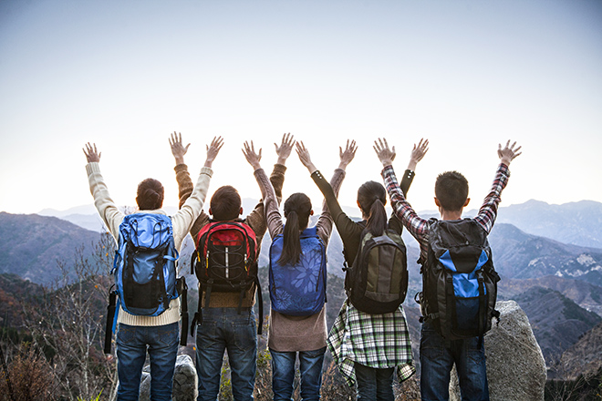 Grupo de jóvenes de espaldas con los brazos en alto en la cima de una montaña