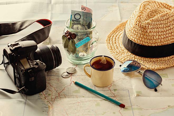 Mapa sobre la mesa con una hucha, cámara fotográfica, infusión y sombrero