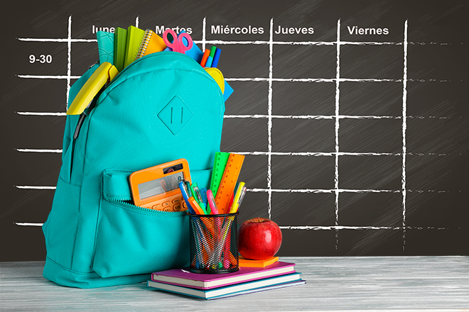 Mochila con accesorios escolares delante de pizarra donde hay un calendario dibujado con tiza