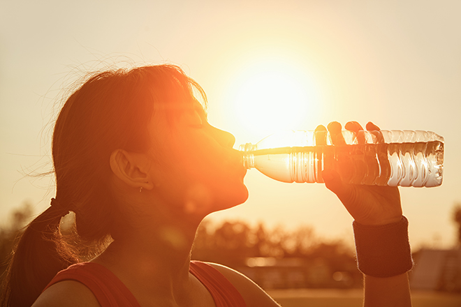 Mujer bebiendo agua de una botella de plástico en entorno natural bajo el sol 