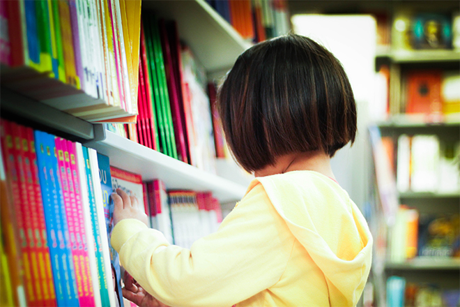 Niña, de lado, cogiendo un libro de texto de una estantería