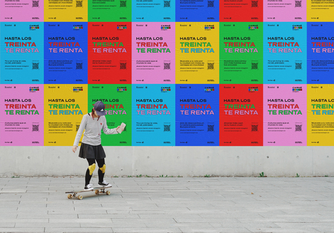 Chica joven sobre un monopatín en una calle que tiene una pared forrada con carteles con el nuevo lema del Carné Joven: Hasta los 30 te renta