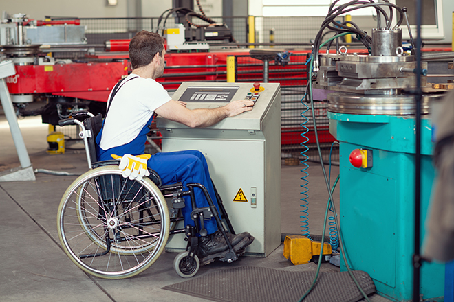 Hombre joven en silla de ruedas delante de una máquina en una fábrica