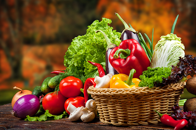 Cesta de mimbre con alimentos vegetales: pimientos verdes y rojos, cebollas, lechugas, tomates, berenjena, pepinos y champiñones