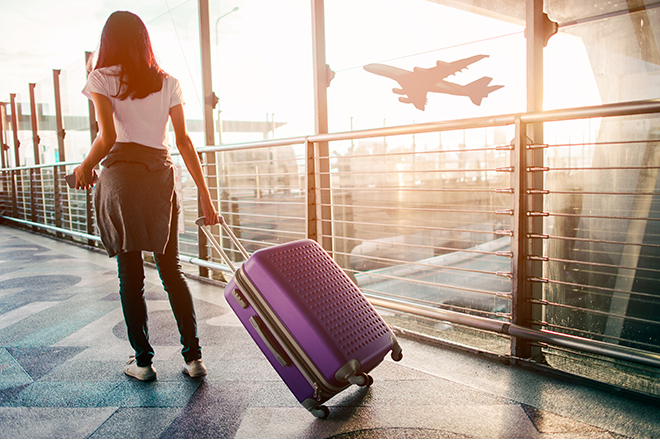Mujer viajando, arrastrando una maleta con ruedas por un aeropuerto