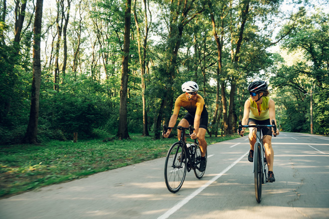Dos ciclistas circulando por una carretera rodeada de árboles y vegetación