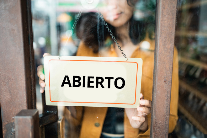 Mujer poniendo el cartel de abierto en la puerta de su tienda